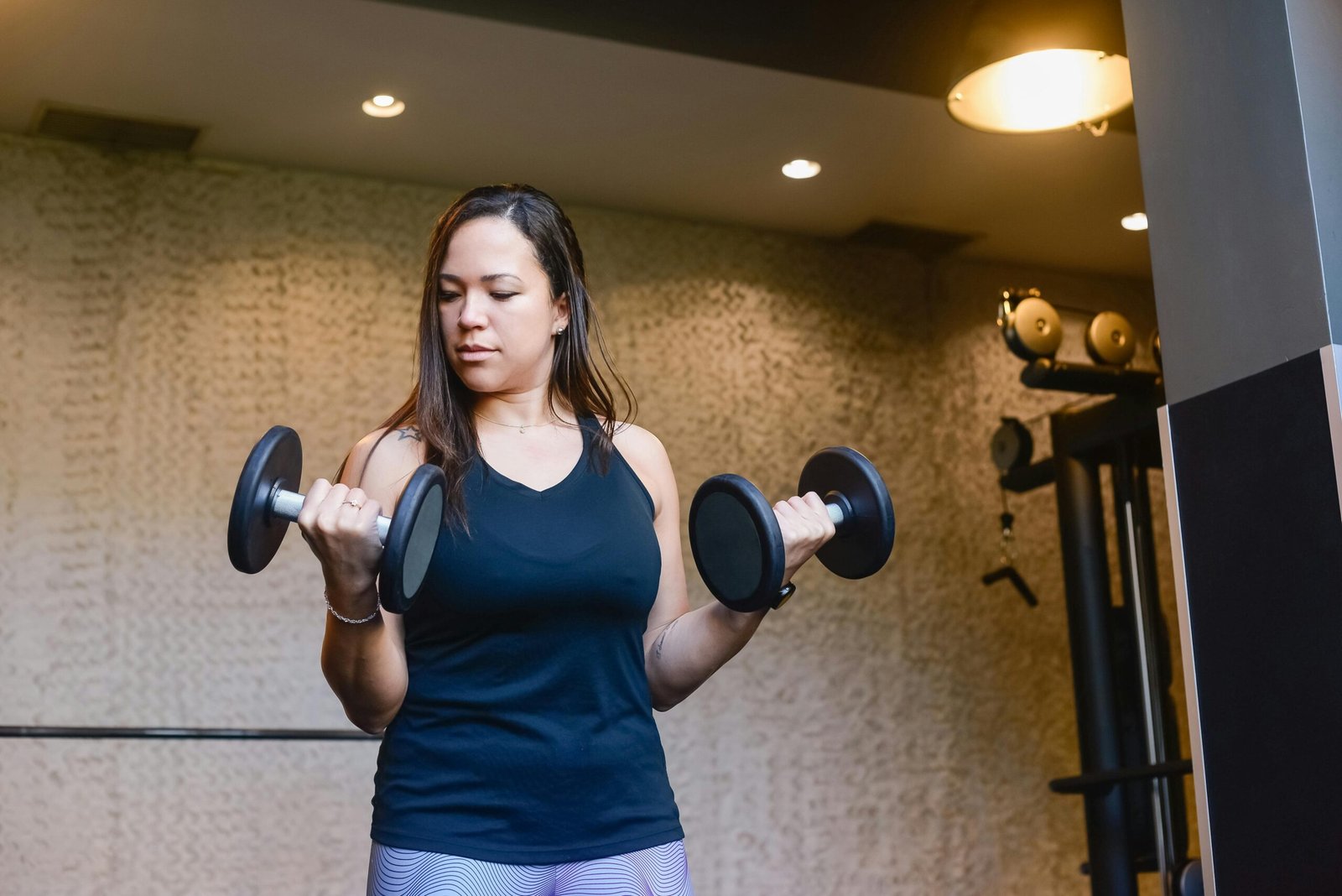 A woman in activewear lifting dumbbells indoors, focused on her workout routine.